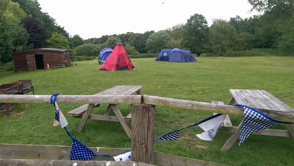 Picnic tables in the foreground, tents and the toilet block in the background showing the whole field as seen from the hut